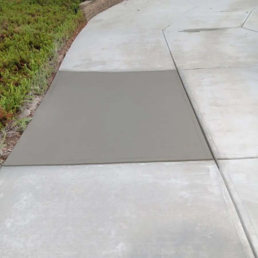 Freshly poured gray concrete on a driveway, with surrounding greenery and textured concrete patterns.