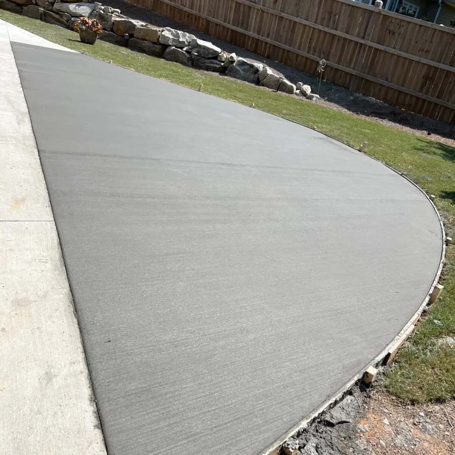 Freshly poured curved concrete driveway with smooth finish and surrounding grass.
