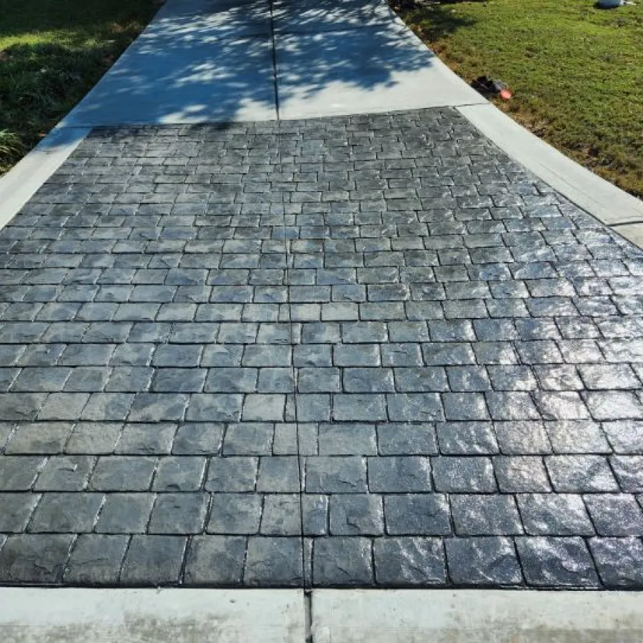 Stamped concrete driveway with a textured stone pattern and smooth concrete border under sunlight.