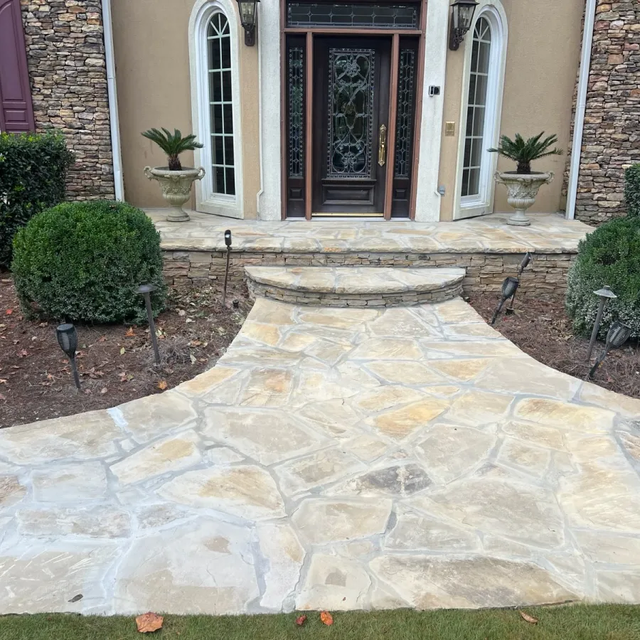 a stone patio with a fountain and bushes in front of a house