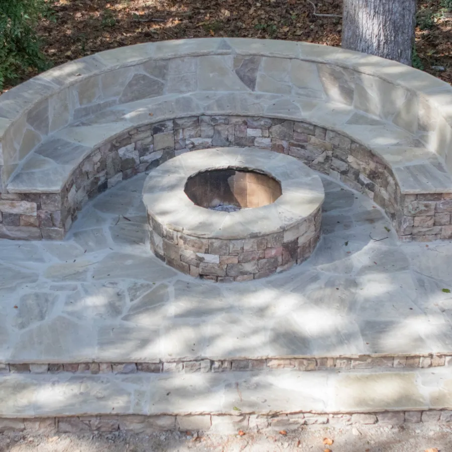 Outdoor stone seating area with a circular fire pit surrounded by curved benches.