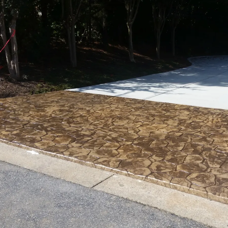 Residential driveway with stamped concrete in stone pattern transitioning to smooth white concrete surrounded by trees.
