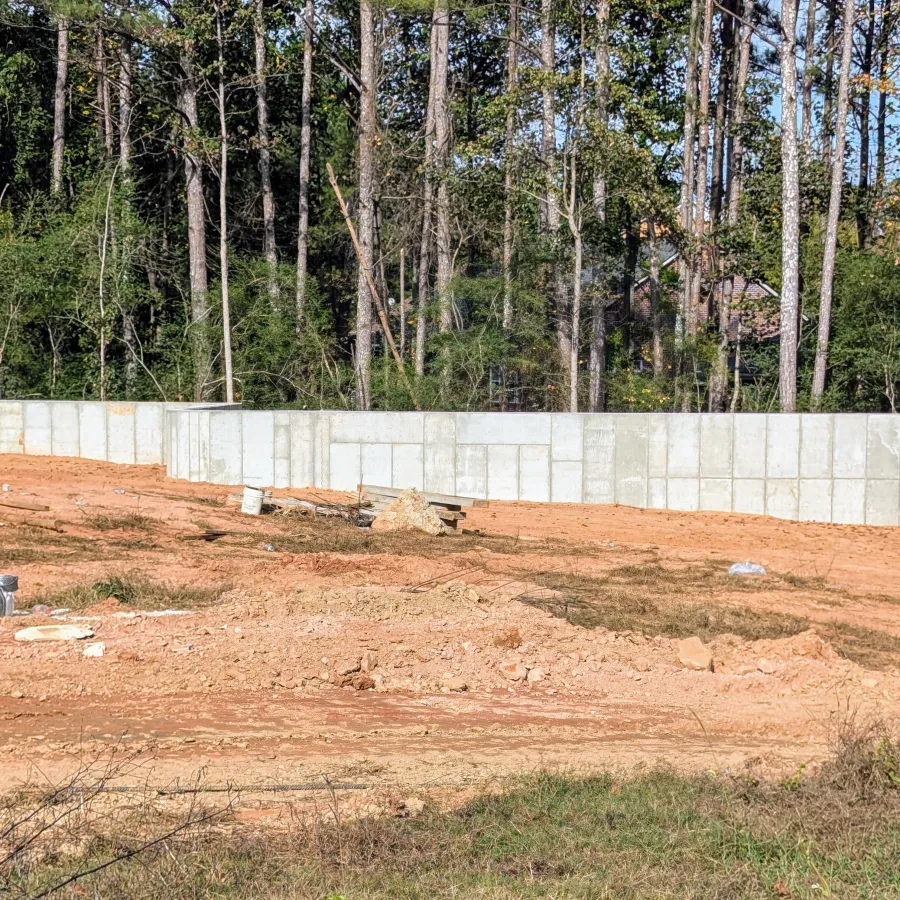 Concrete retaining wall built on cleared red dirt land with dense forest in background on a sunny day
