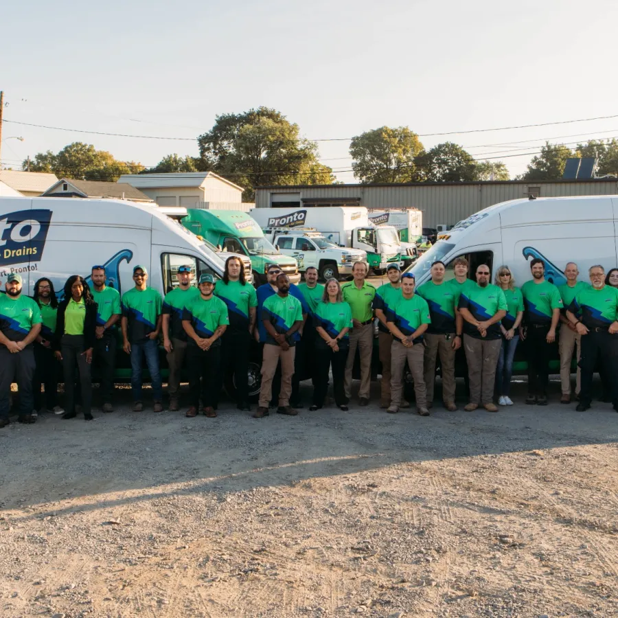 Pronto service team in matching green shirts standing in front of branded service vans at outdoor company lot.