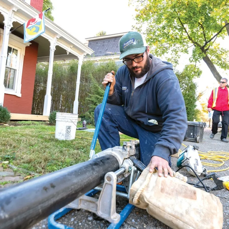 Technician using pipe fusion machine to join black plastic pipes outdoors near residential area.