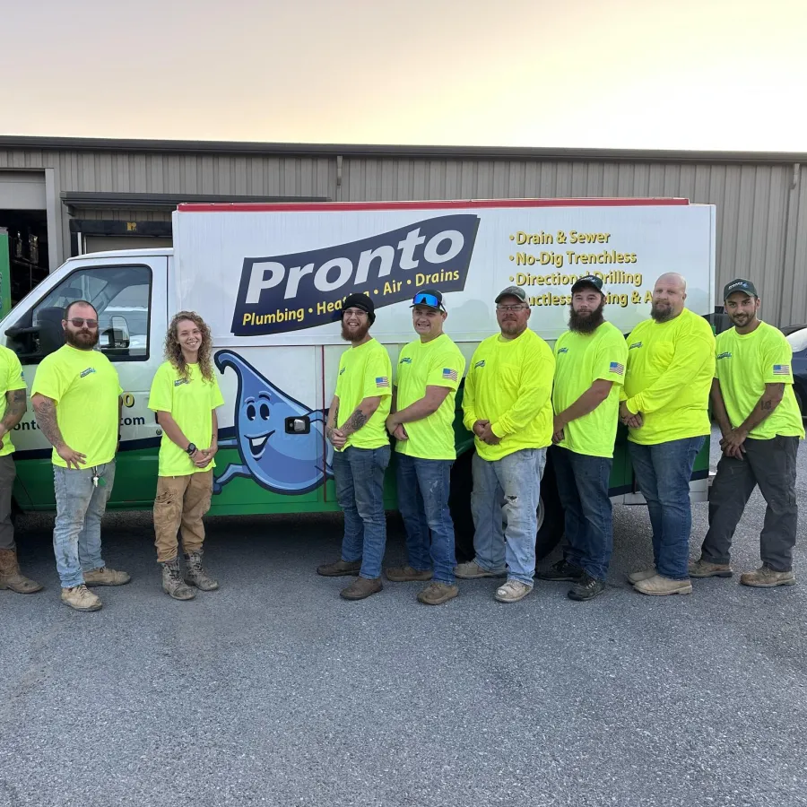 Pronto Plumbing team in neon yellow shirts standing in front of company trucks outside a building at sunset