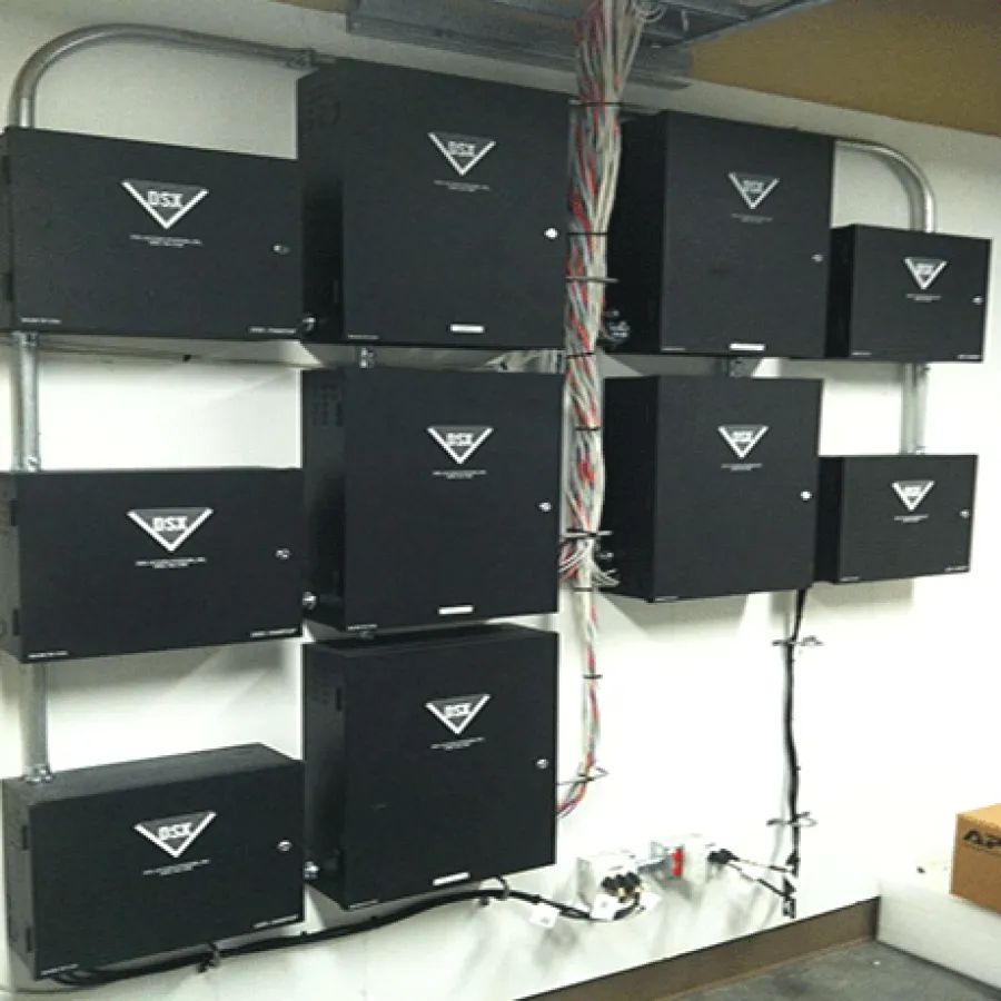 Wall-mounted black network control panels with organized cables in a utility room with concrete floor and yellow wall.