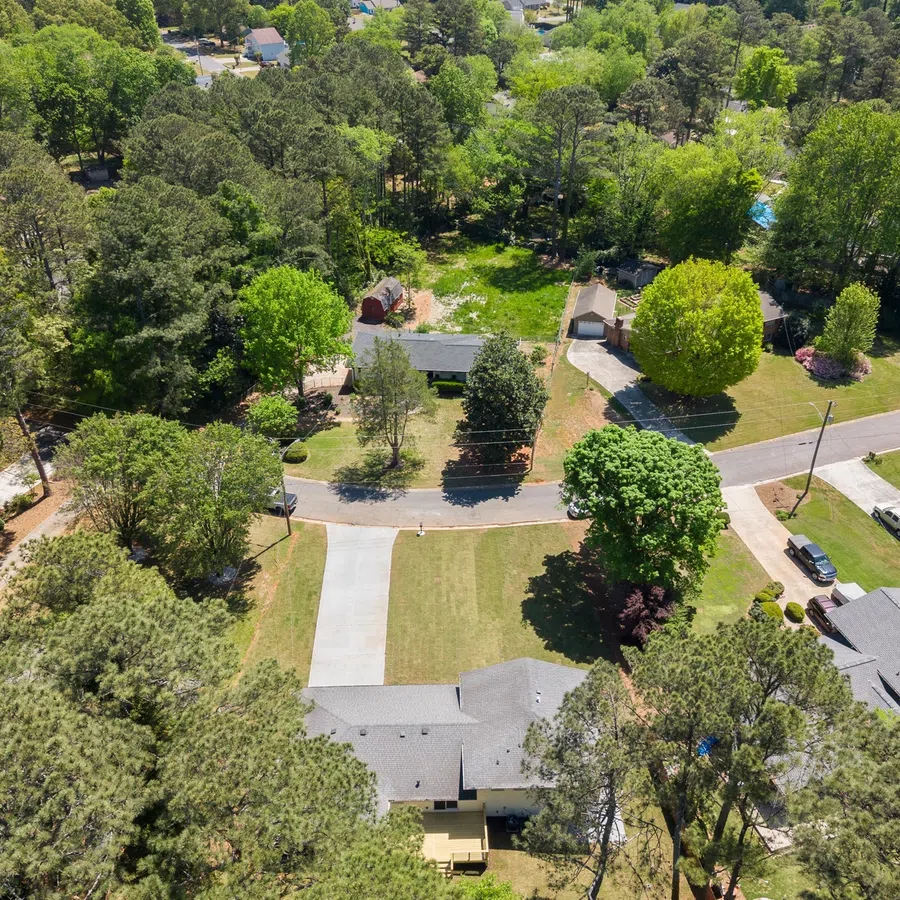 Aerial view of suburban neighborhood with houses, trees, lawns, and a circular street on a sunny day.