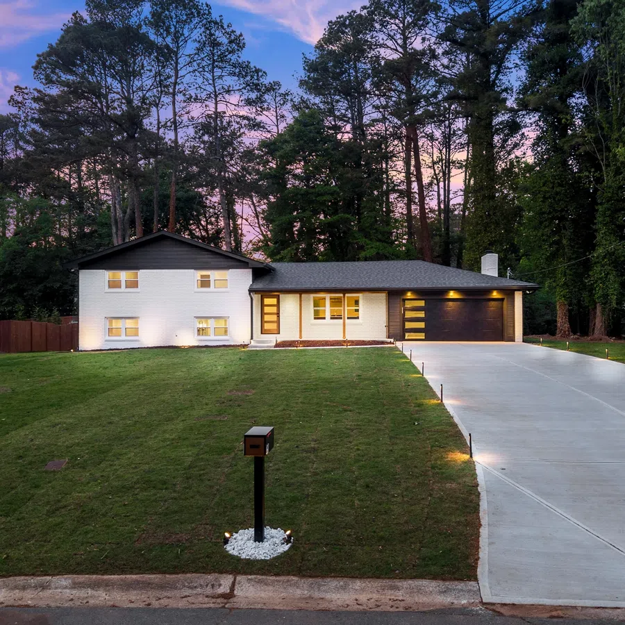 Modern white house with large driveway and green lawn at dusk surrounded by tall pine trees