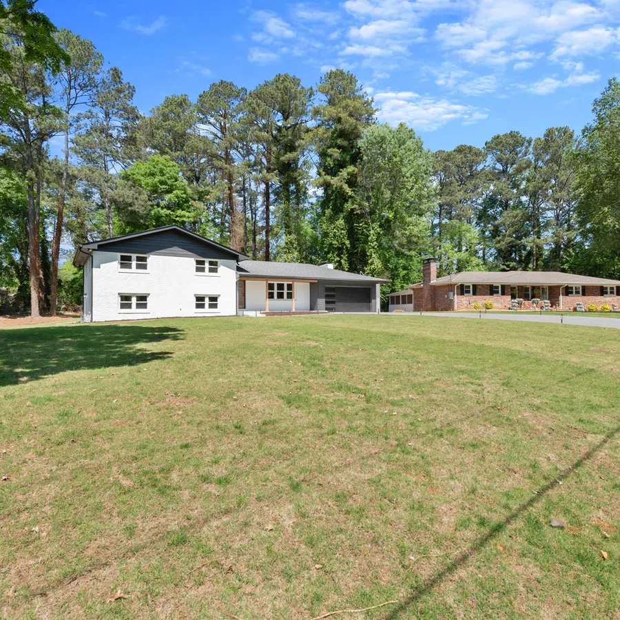 Two suburban houses with spacious green lawns and tall trees under a clear blue sky on a sunny day