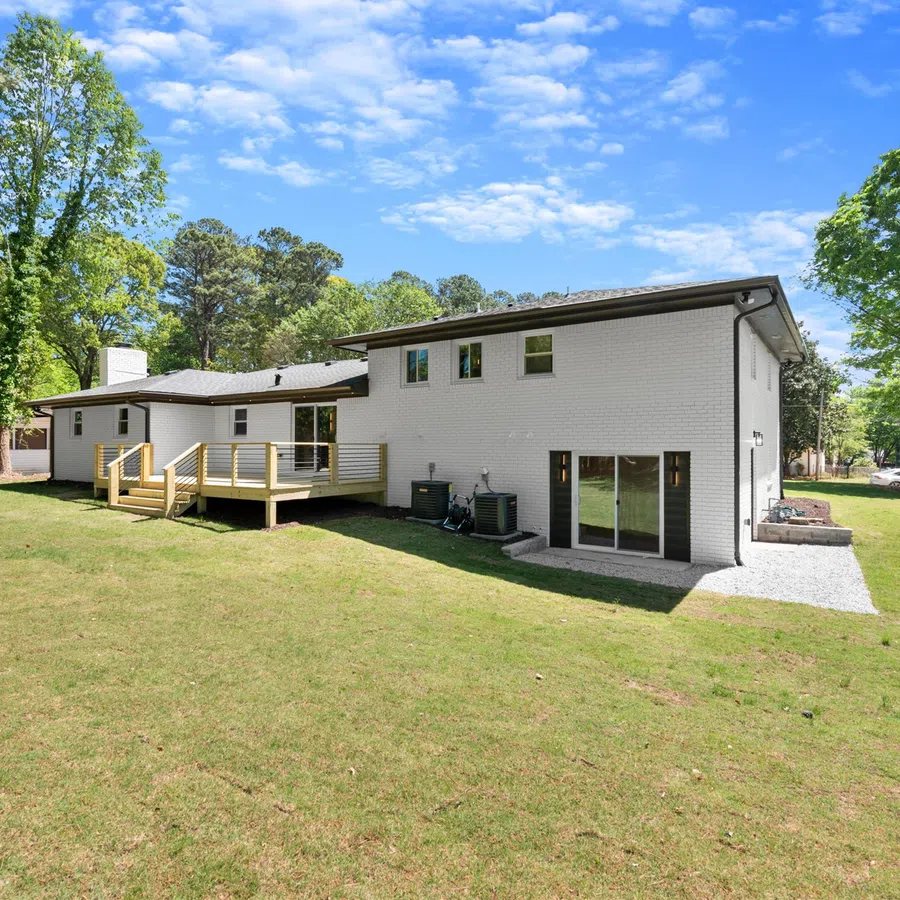 Modern white brick two-story house with a spacious backyard and wooden deck under a sunny blue sky.