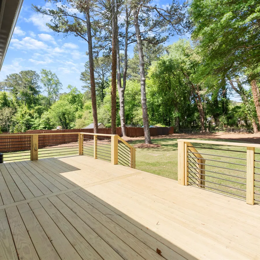 Spacious wooden outdoor deck with metal railing overlooks a green yard with tall trees under a clear sky