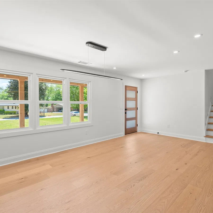 Bright empty room with large windows, wooden floor, white walls, modern ceiling light, and staircase.