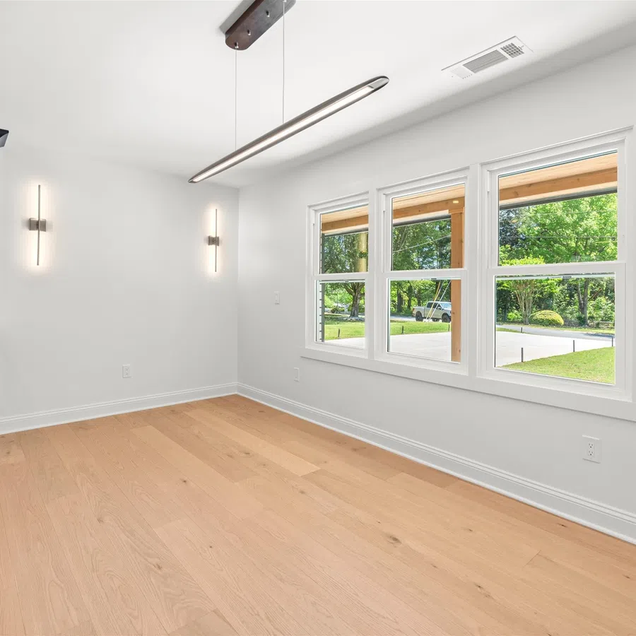 Bright modern room with light wood flooring, black cabinets, white walls, and large windows with outdoor view