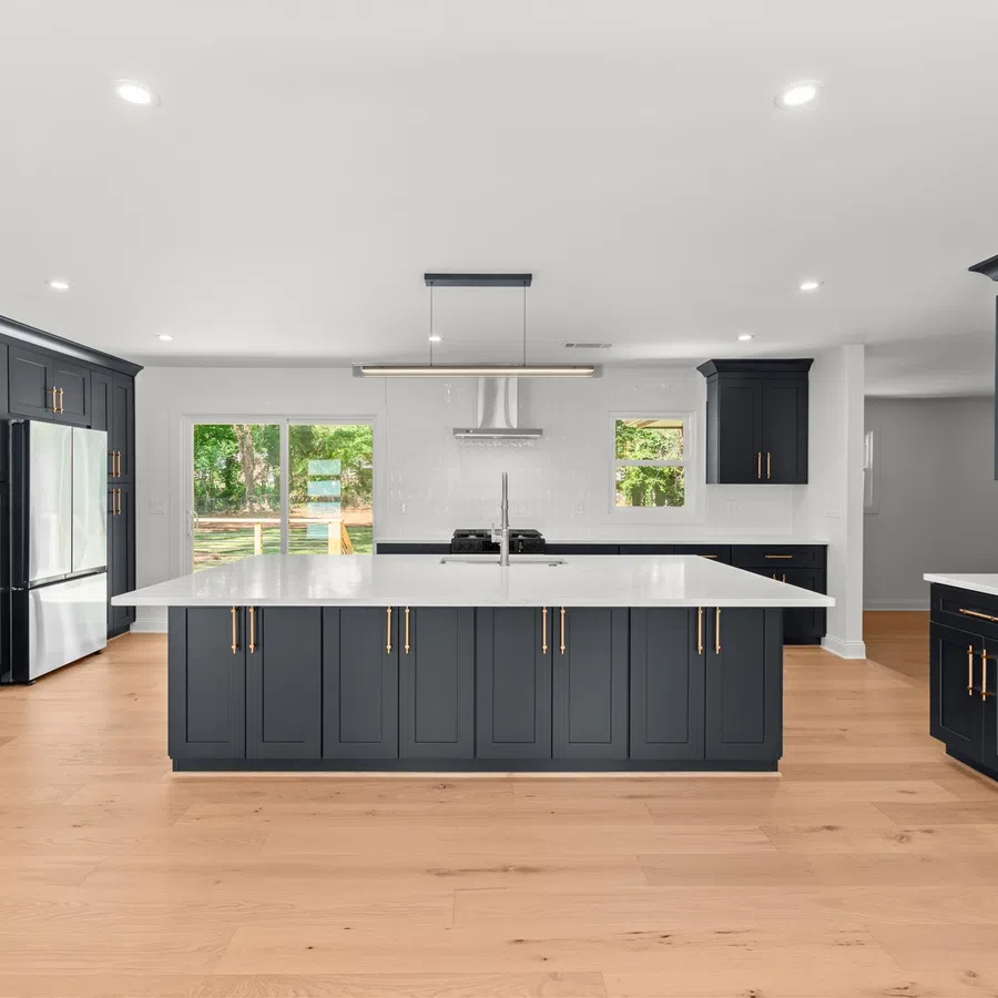 Modern kitchen with dark gray cabinets, large white island, stainless appliances, and wood flooring under natural light