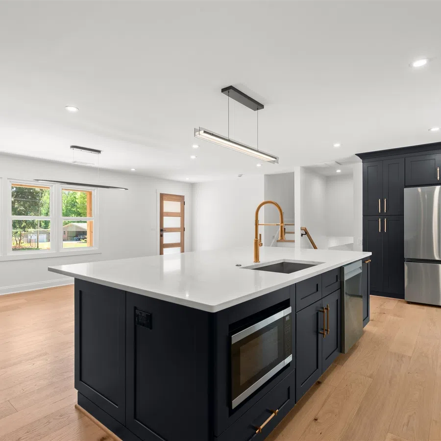 Modern kitchen with black cabinetry, white countertops, large island, gold fixtures, stainless steel appliances, and wood flooring.