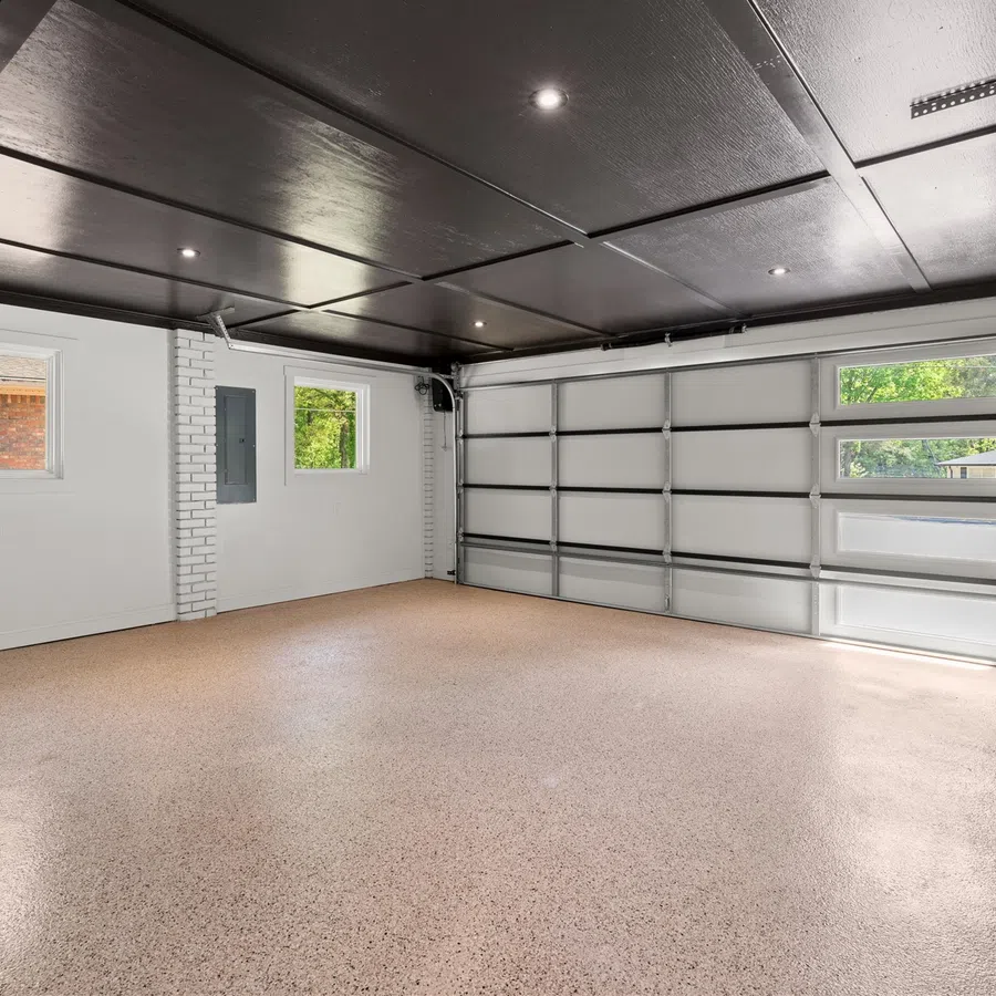 Empty clean garage with polished floor, white brick walls, windows, and a closed sectional garage door.