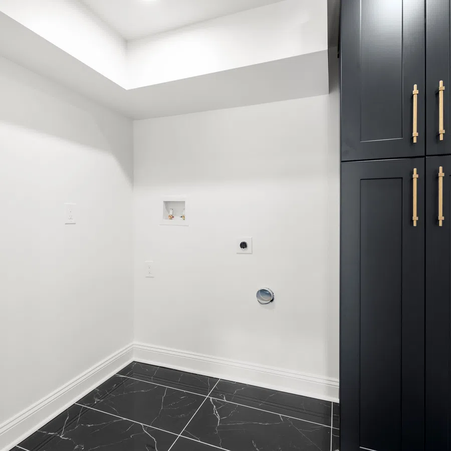 Minimalist laundry room with black marble floor tiles and a tall black storage cabinet with gold handles.