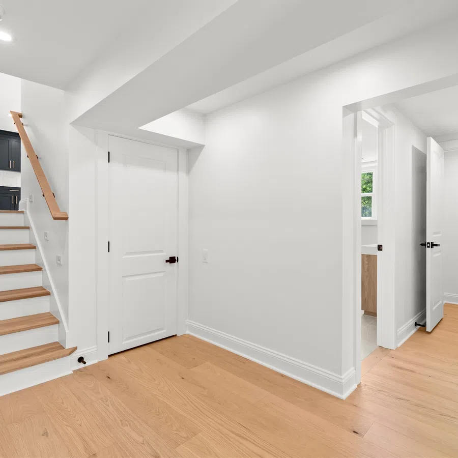 Bright interior hallway with light wood floors, white walls, staircase leading to a kitchen with black cabinets.