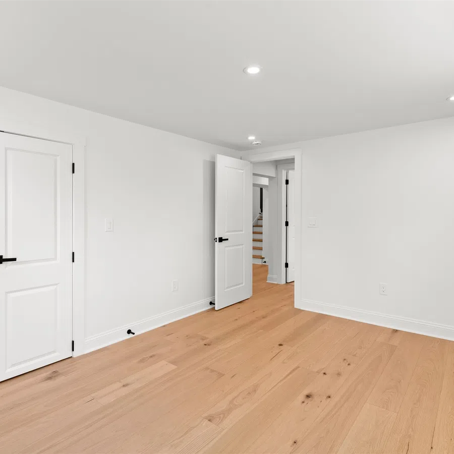Empty white room with light wood flooring, white doors, and recessed ceiling lights in a modern home.