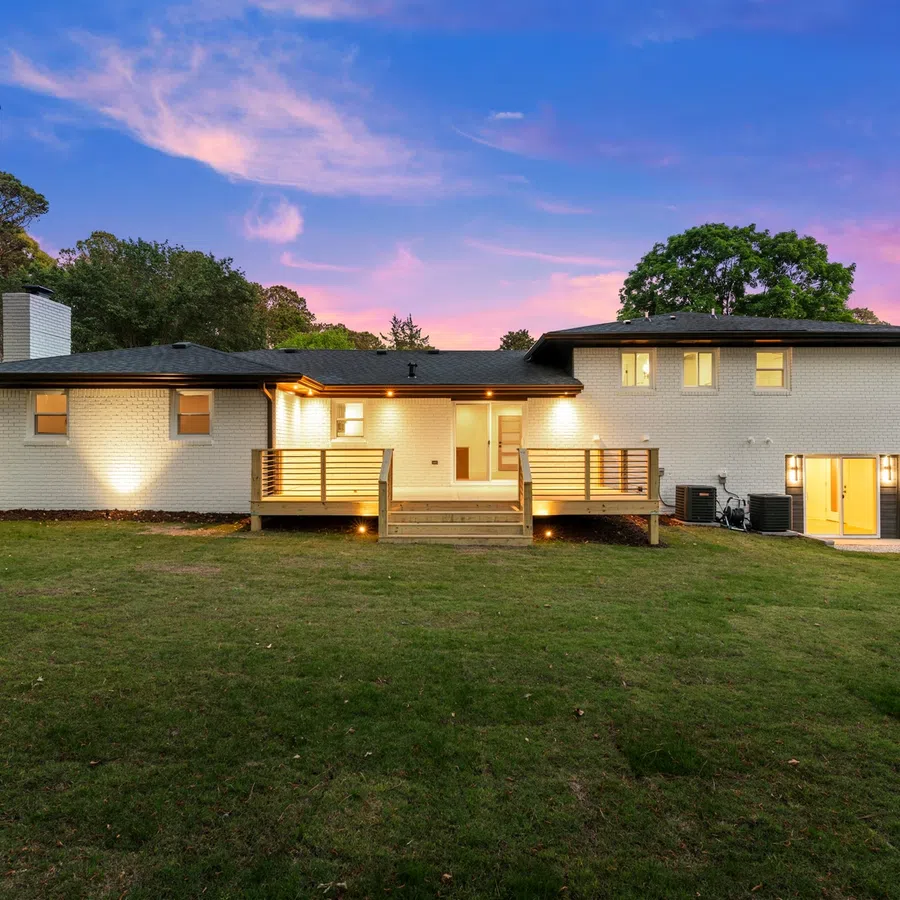Modern two-story brick house with illuminated deck and spacious green lawn at sunset under a vibrant sky