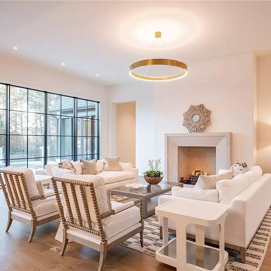 Bright modern living room with white sofas, wooden armchairs, fireplace, large windows, and circular ceiling light