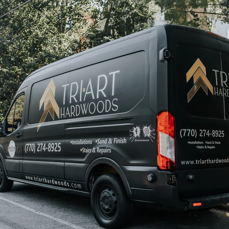 Black TriArt Hardwoods van parked on a street with company logo and contact details visible on the side and back.