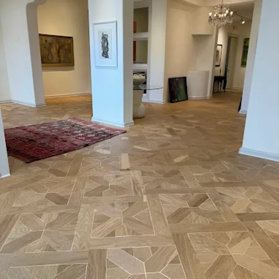 Intricate wooden parquet flooring in a bright art gallery with white walls and framed artwork.