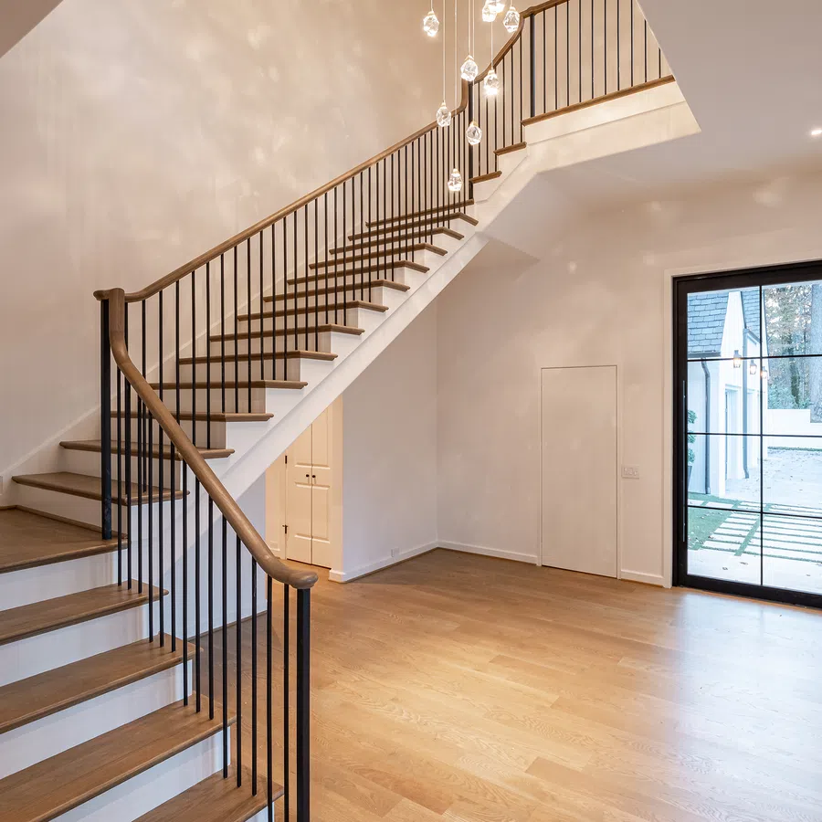 Modern interior with wooden staircase, black metal railing, hardwood floor, and large glass door leading outside