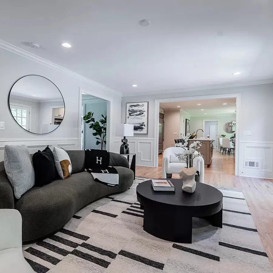 Bright modern living room with curved dark sofa, round black coffee table, patterned rug, and fireplace with glass doors.