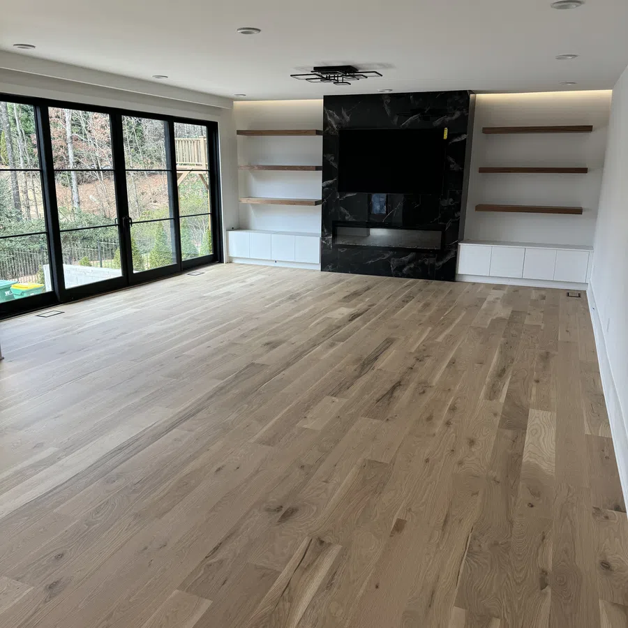 Spacious living room with light wood flooring, black framed glass doors, black marble TV wall, and built-in shelves.