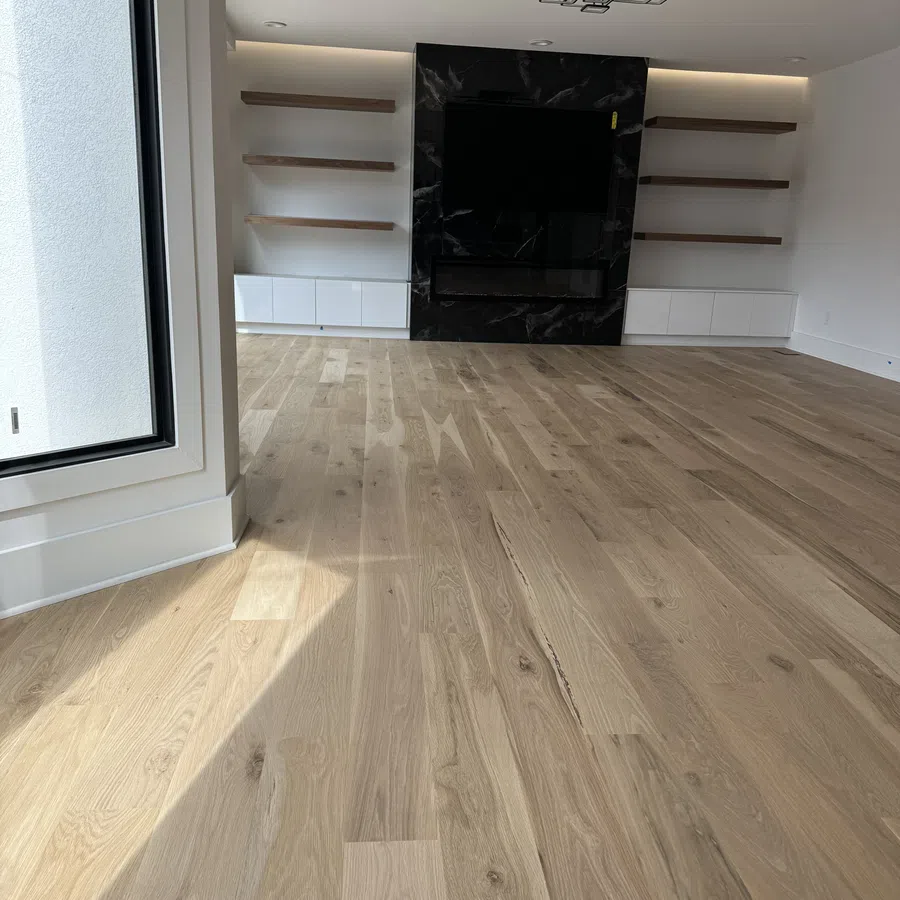 Modern living room with light oak hardwood floors, black marble TV wall, floating shelves, and large window.