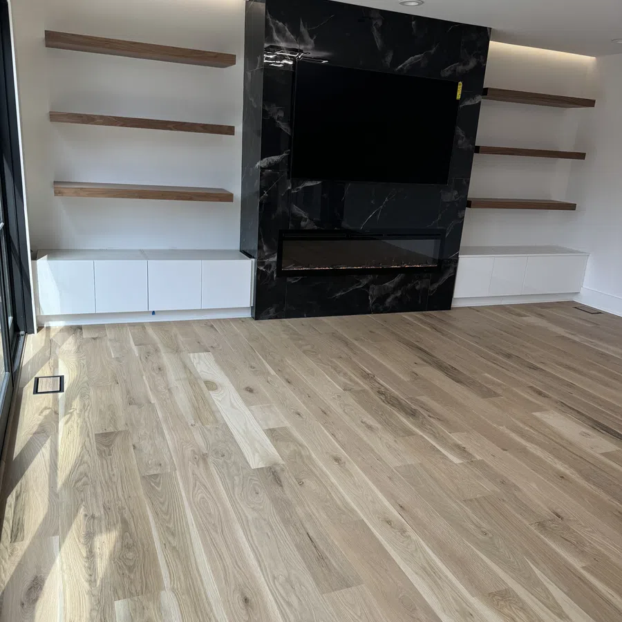 Modern living room with light wood flooring, floating wooden shelves, black marble TV wall, and white cabinets.