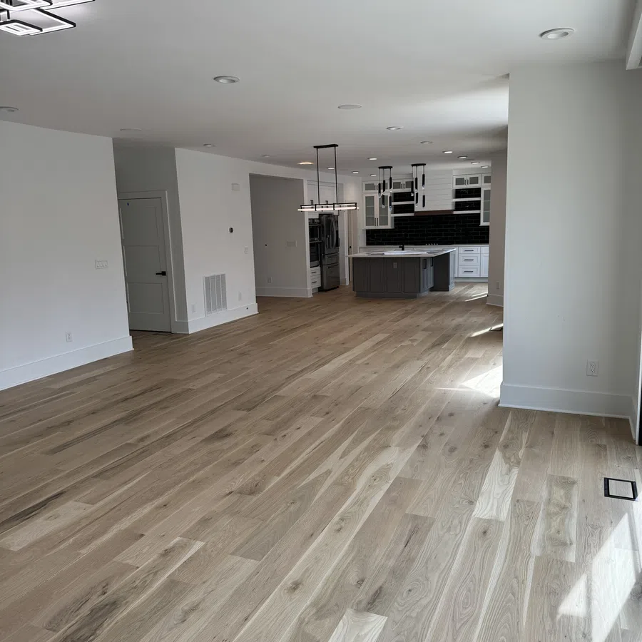 Spacious modern open-concept room with light hardwood floors, white walls, and a kitchen featuring gray cabinets and black backsplash.