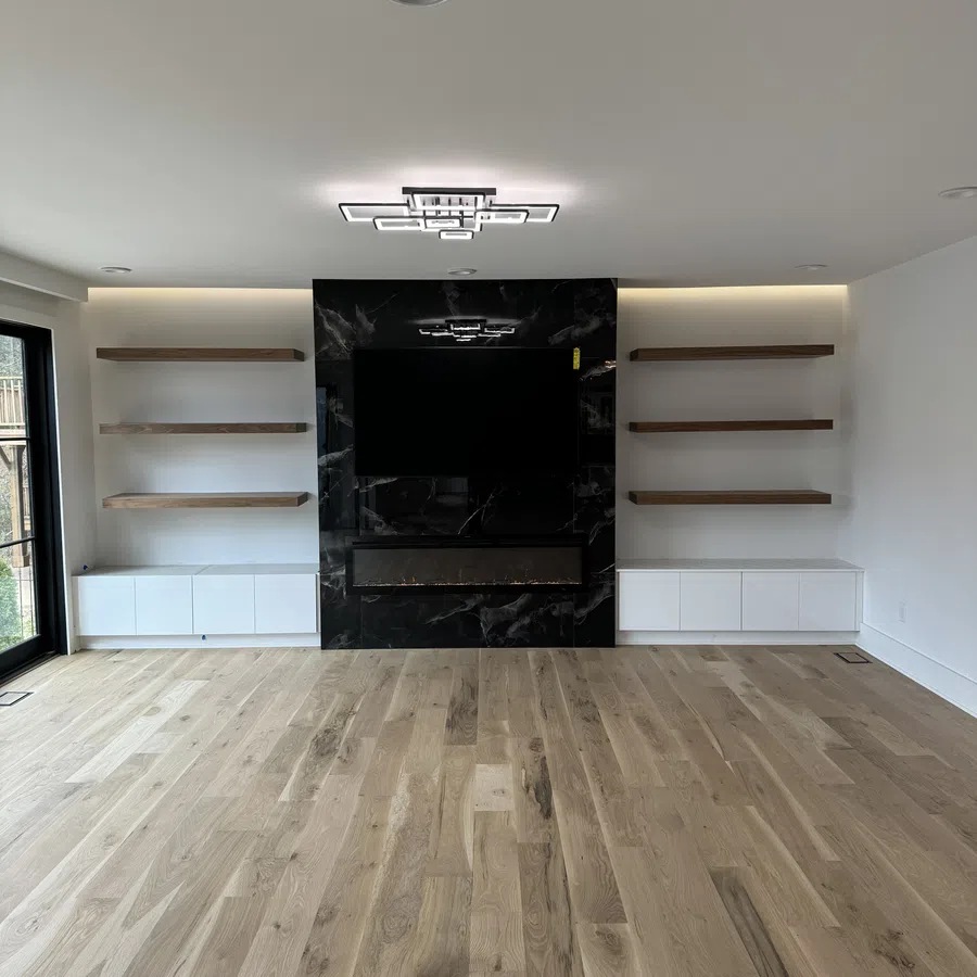 Modern living room with light wood flooring, black marble TV wall, floating shelves, and white cabinets.