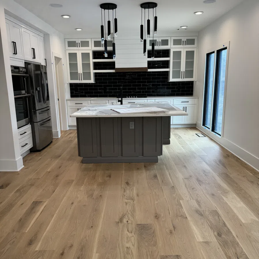 Modern kitchen with white cabinets, black subway tile backsplash, gray island, wood flooring, and pendant lights.