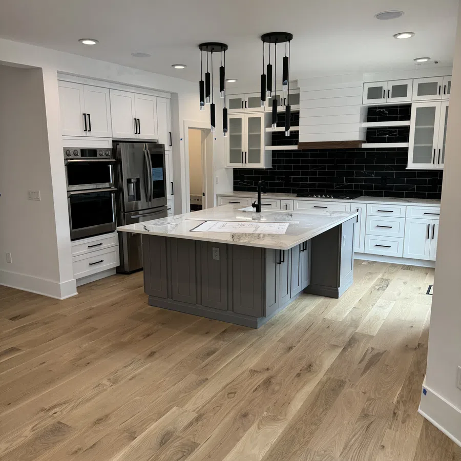 Modern kitchen with white cabinets, black backsplash, gray island with marble countertop, and wood flooring.