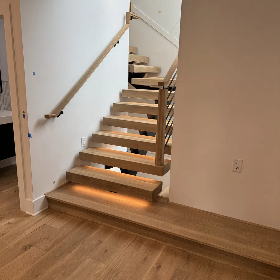 Modern wooden floating staircase with under-step lighting and minimalist white walls in a clean interior.