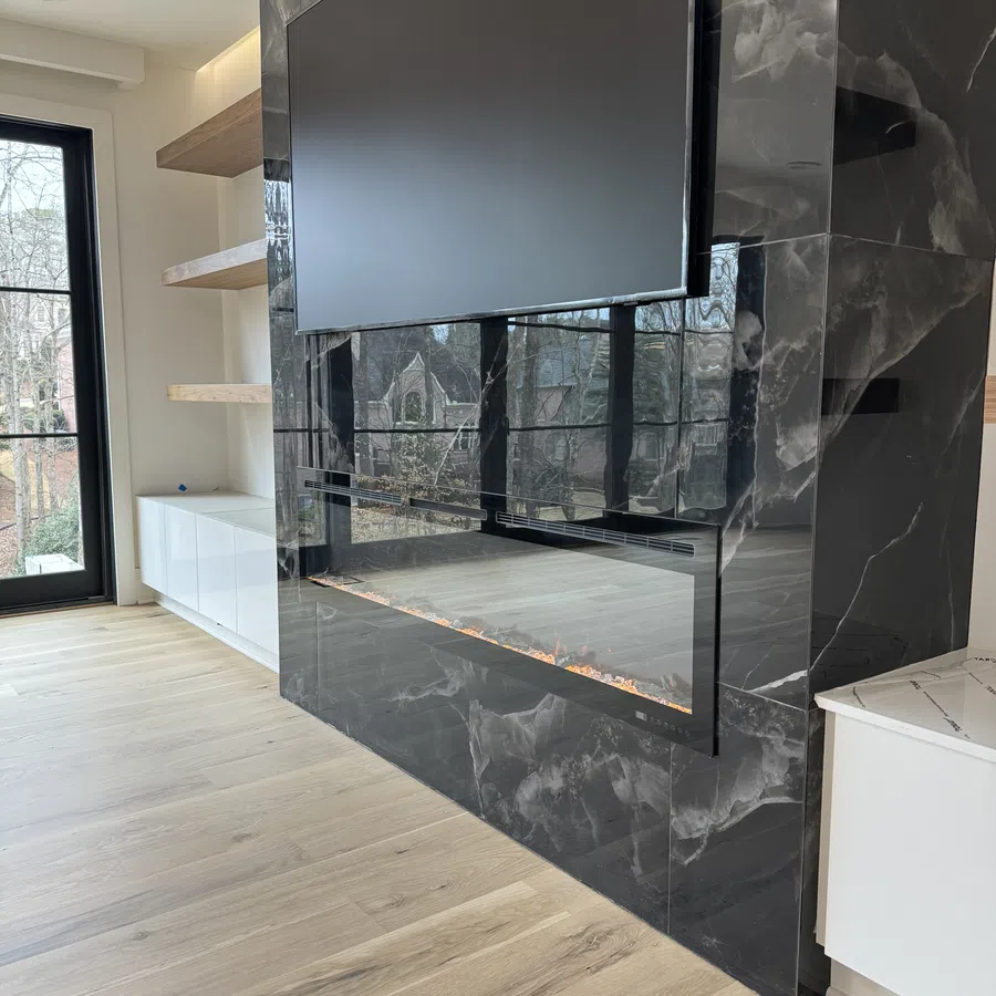 Modern black marble electric fireplace with mounted flat screen TV in a bright living room with wooden floors.