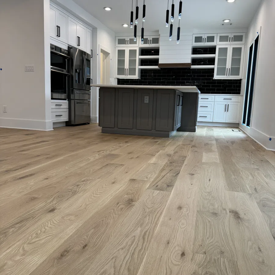 Modern kitchen with wooden floors, gray island, white cabinets, black backsplash, and pendant lighting.