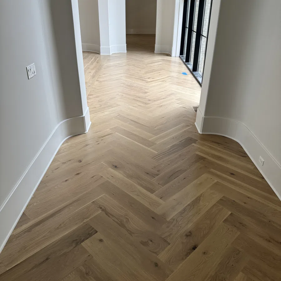 Empty hallway with light herringbone wood flooring, white walls, curved baseboards, and arched doorway.