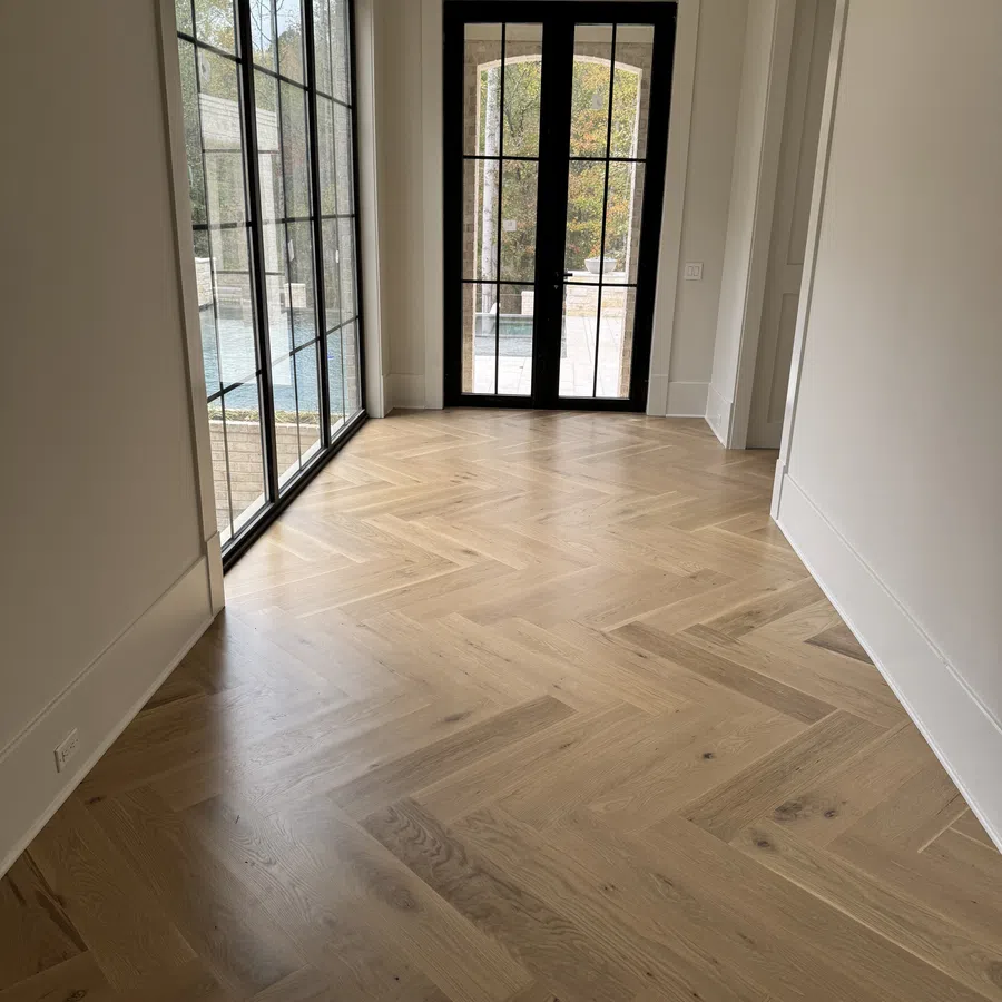 Bright hallway with herringbone wood floor, large black-framed glass doors and windows opening to outdoor view.