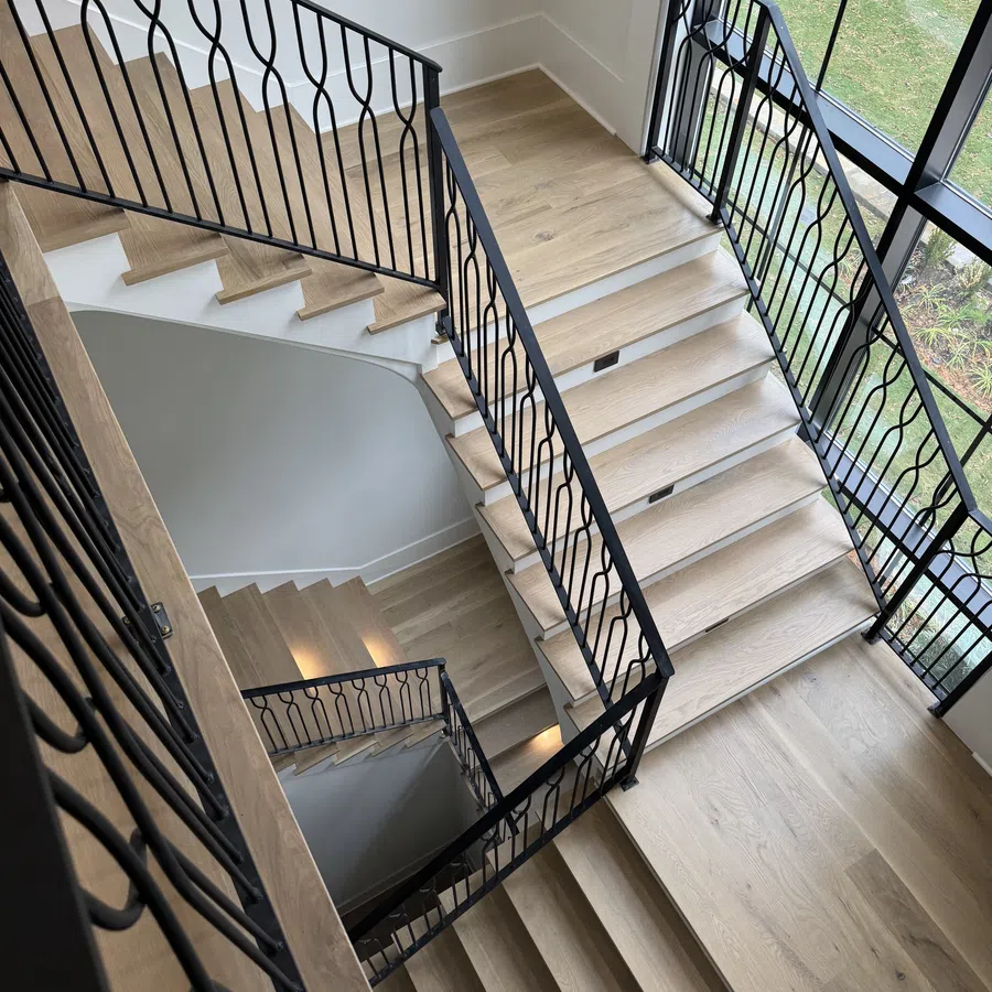 Modern wooden staircase with black metal railings inside a bright room with large windows
