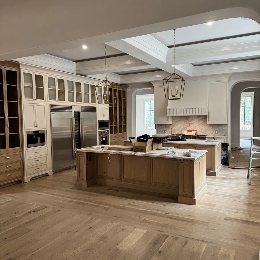 Spacious modern kitchen with wooden floors, large island, stainless steel appliances, and white cabinetry with glass doors.