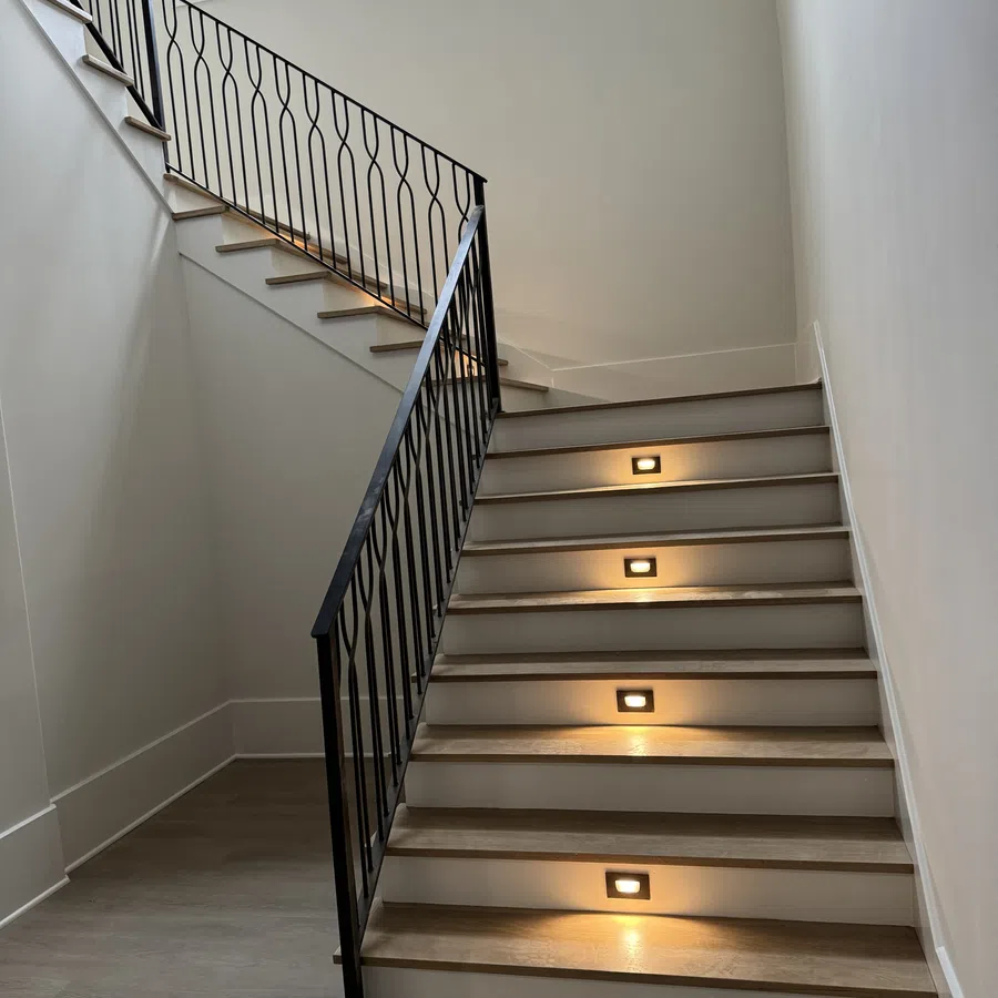 Modern indoor staircase with wooden steps, black metal railing, and built-in step lights in a bright space.