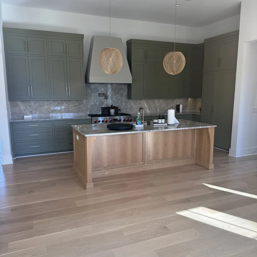 Modern kitchen with green cabinets, wooden island, marble countertops, and two pendant lights over the island.