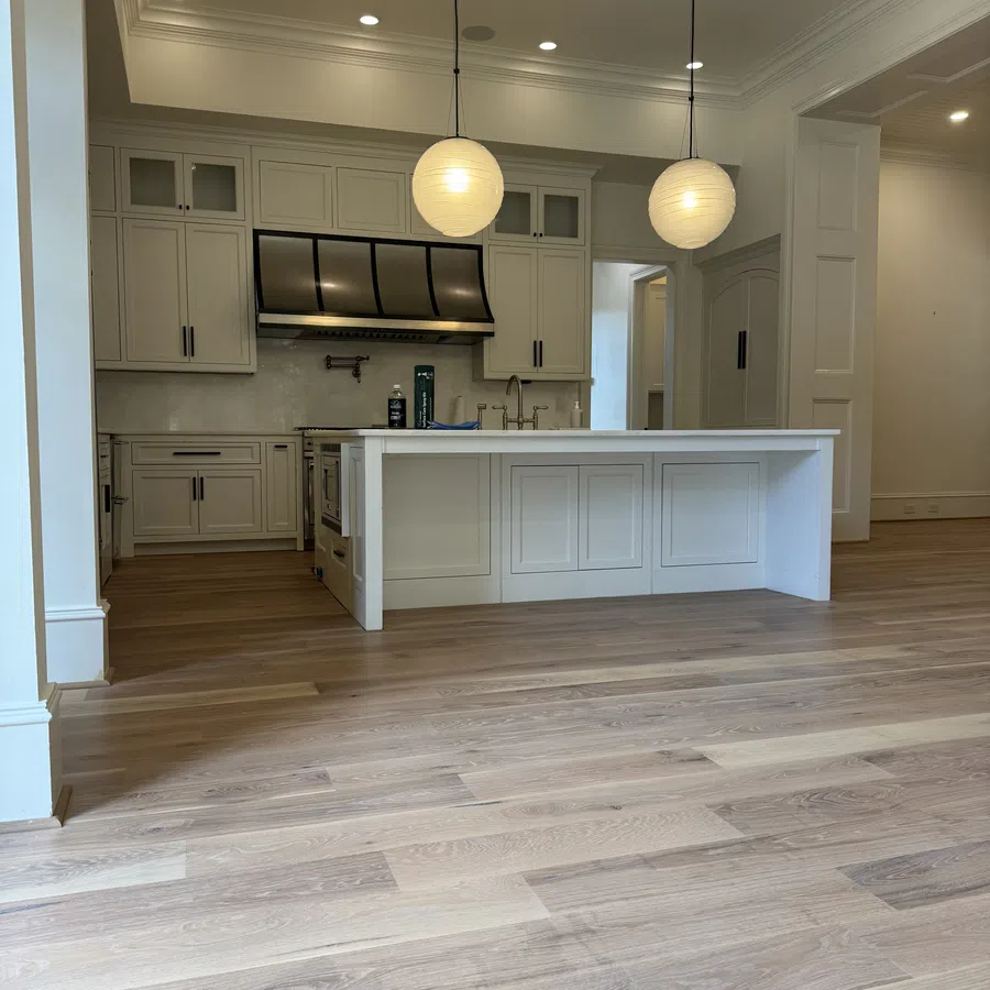 Modern kitchen with hardwood floors, white cabinetry, central island, and two round pendant lights.