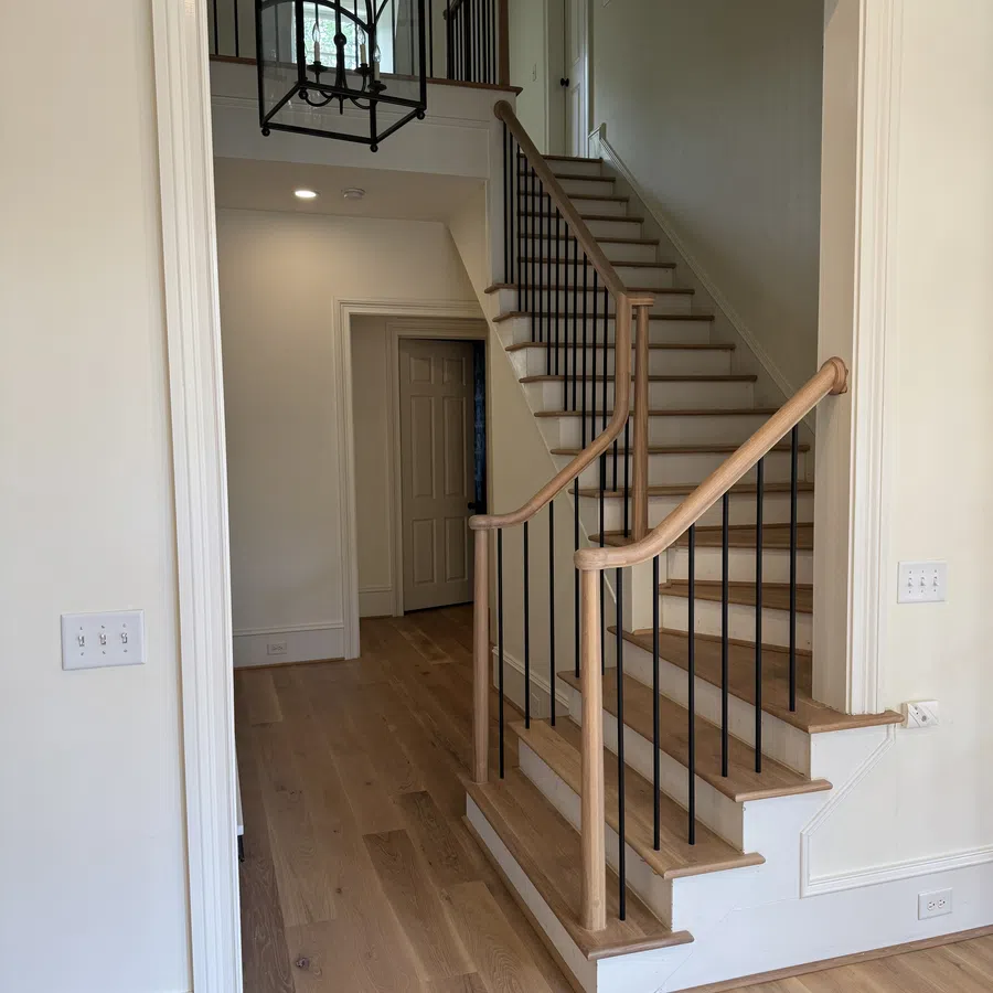 Modern wooden staircase with black metal balusters in a bright home interior with hardwood floors.