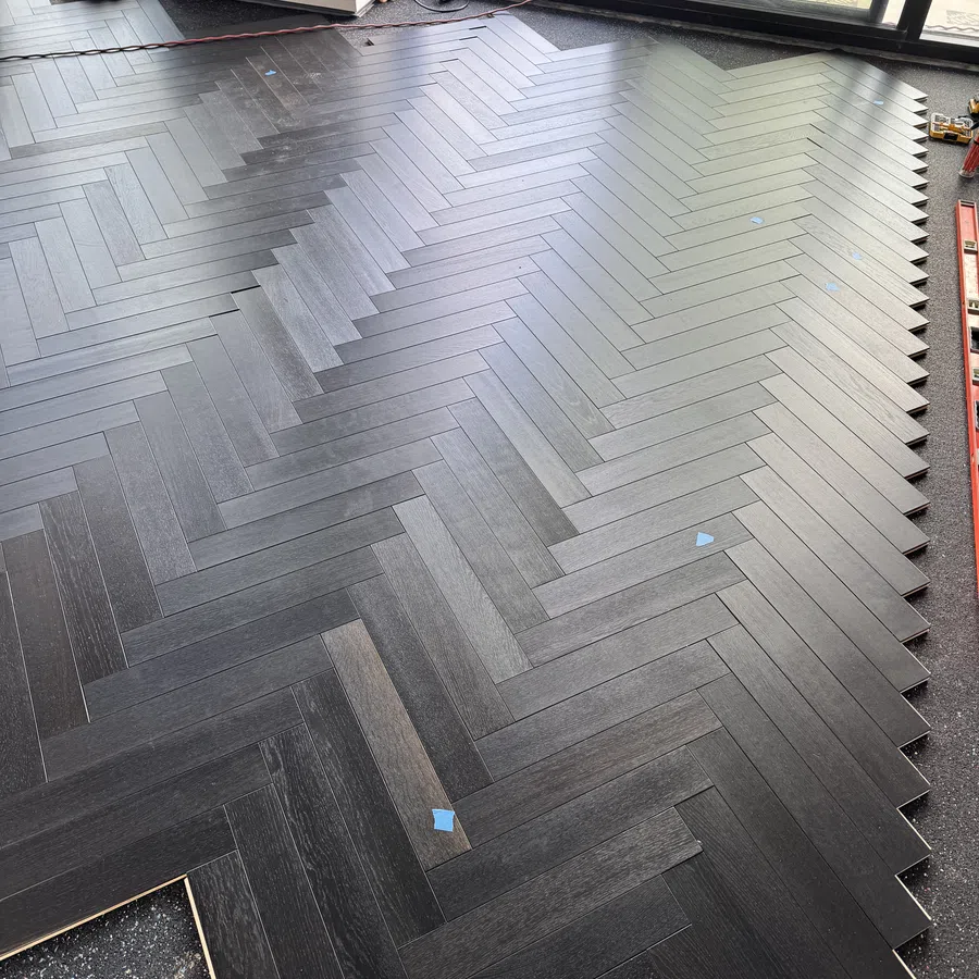 Dark wood floor with herringbone pattern partially installed in a room with large windows and construction tools.