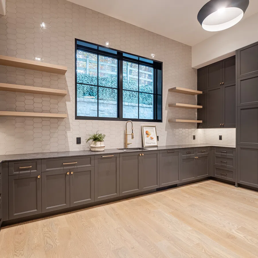 Modern kitchen with gray cabinets, light wood flooring, open shelves, and a large window with natural light.